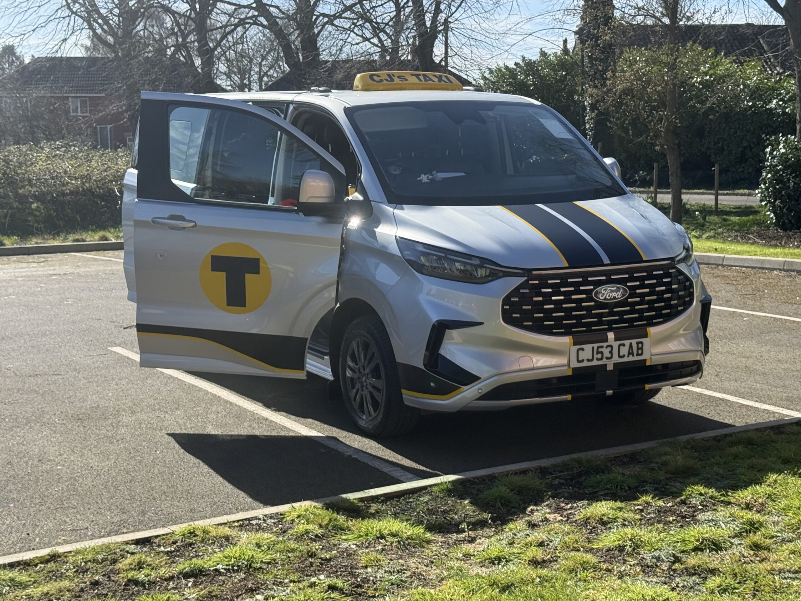 Silver CJ’s Taxi Ford with black and yellow branding and its front passenger door open.